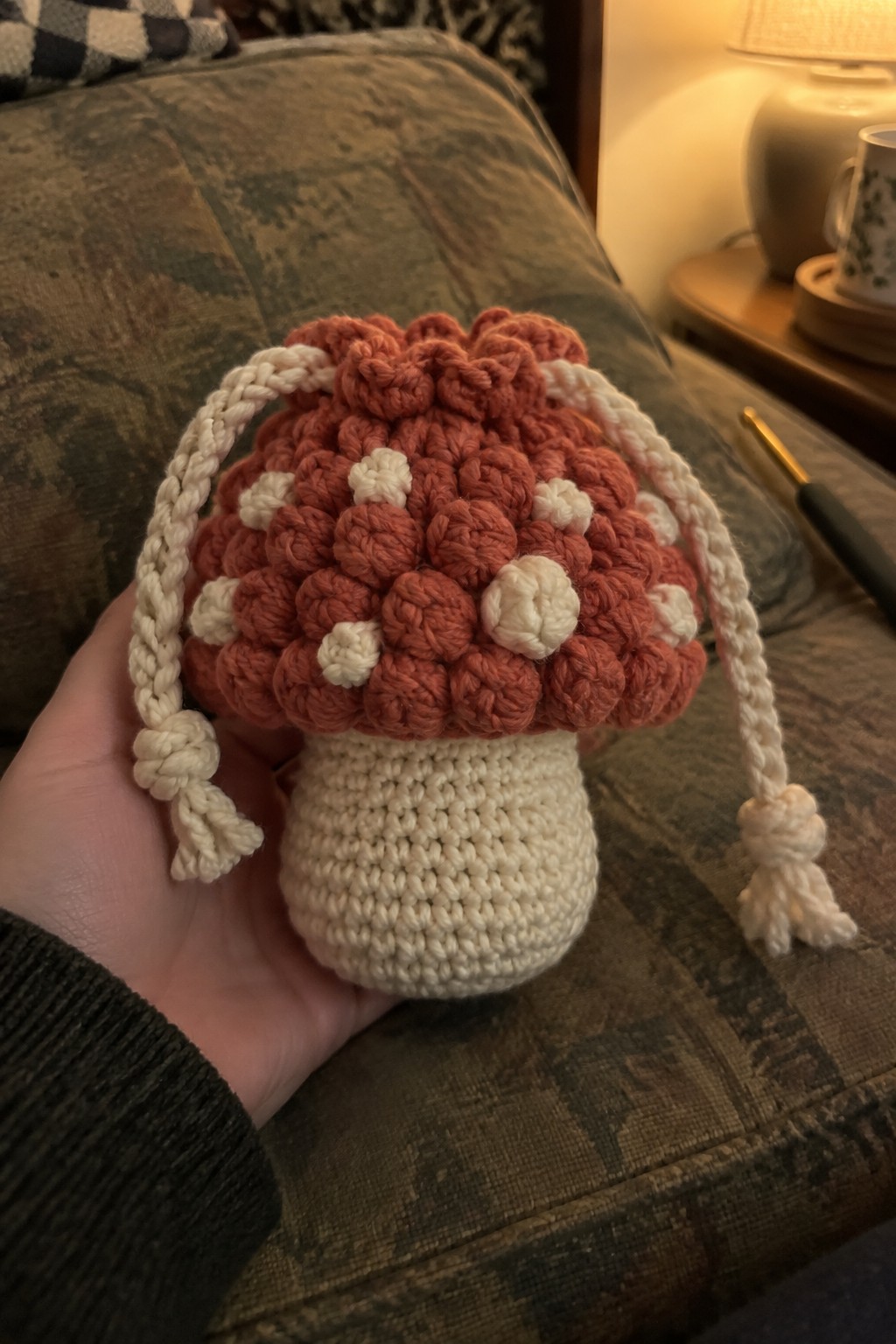 Hand holding crocheted orange mushroom pouch with white spots and drawstrings