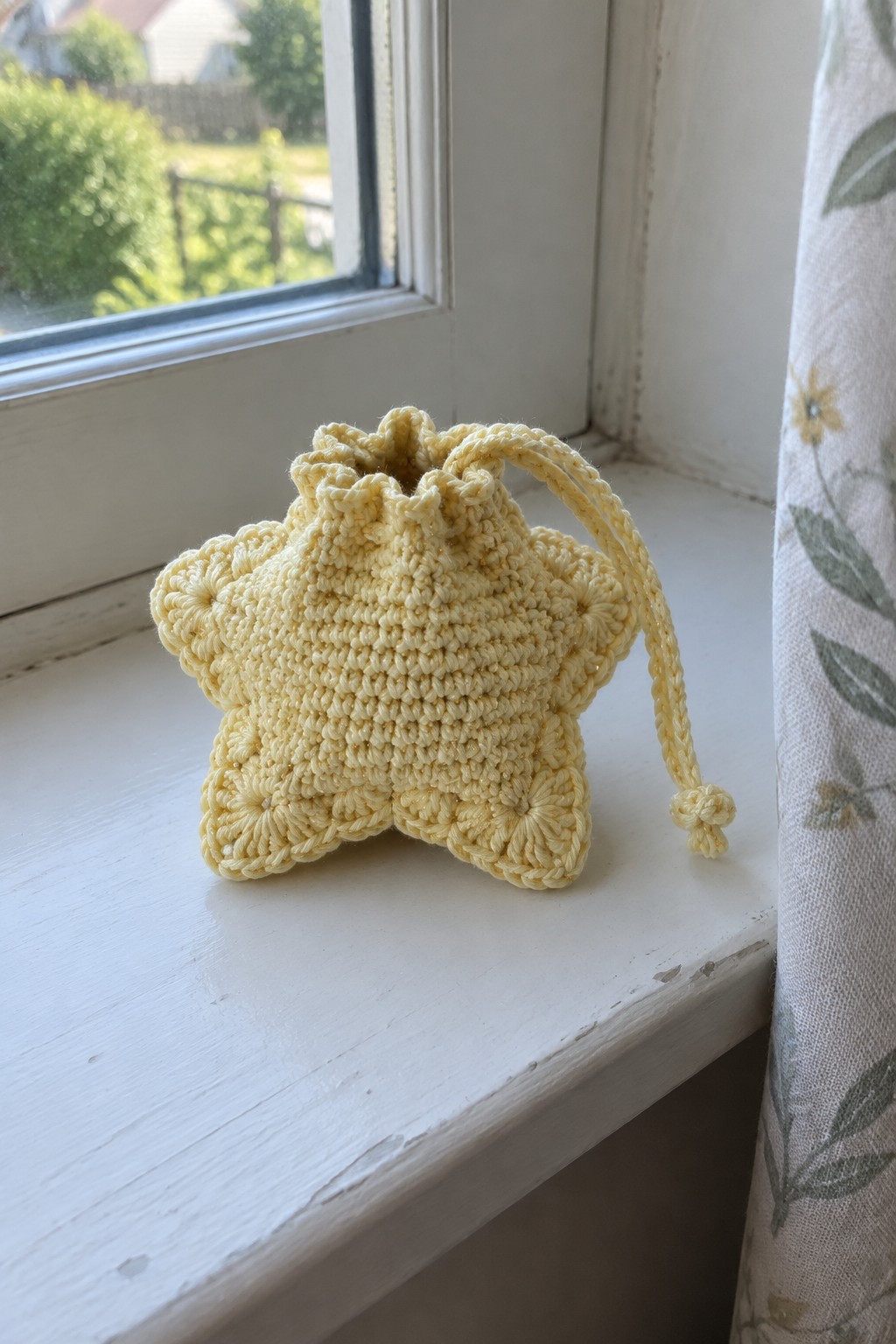 Yellow crocheted star-shaped drawstring pouch on white windowsill by window