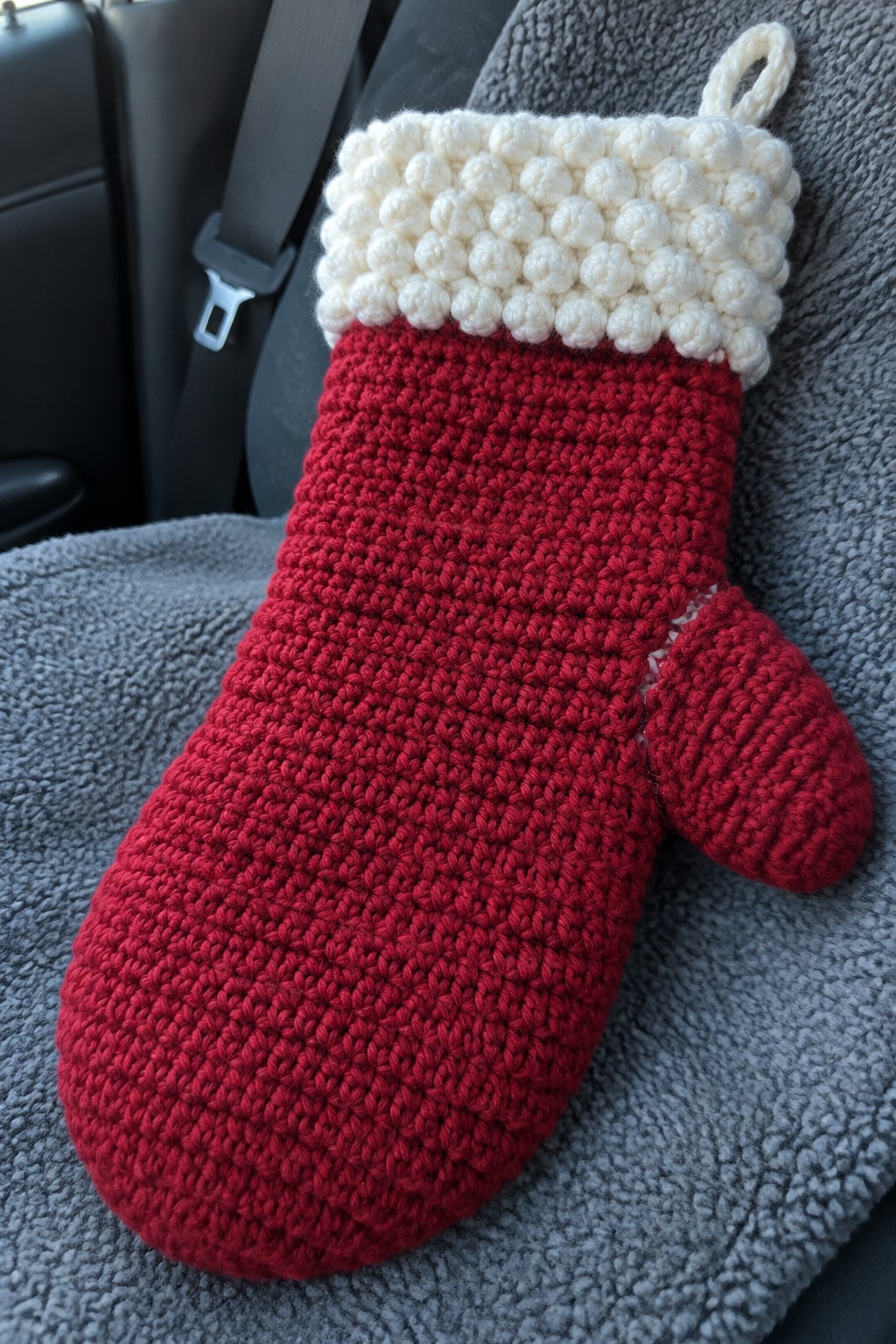 Red knitted Christmas stocking with white bobble cuff on gray car seat.
