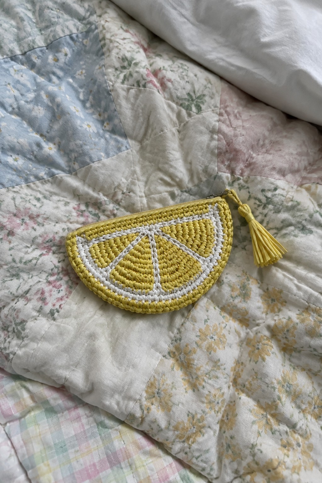 Yellow crocheted lemon pouch with tassel on floral patchwork quilt
