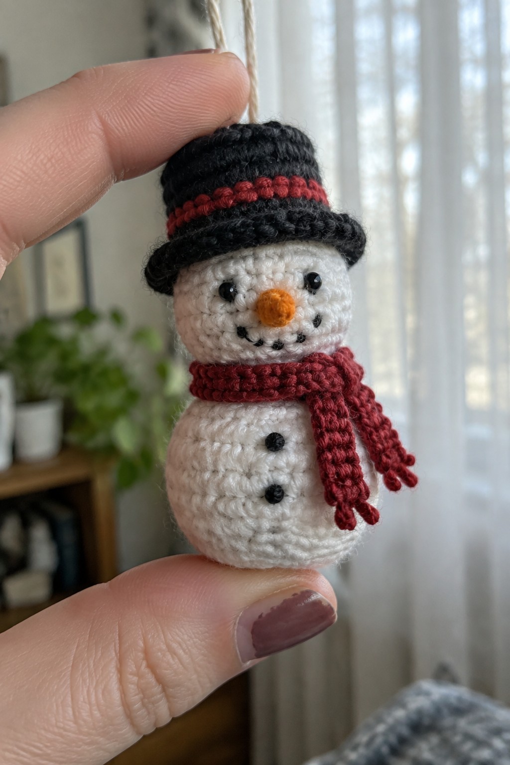 Hand holding crocheted snowman ornament with black hat and red scarf.