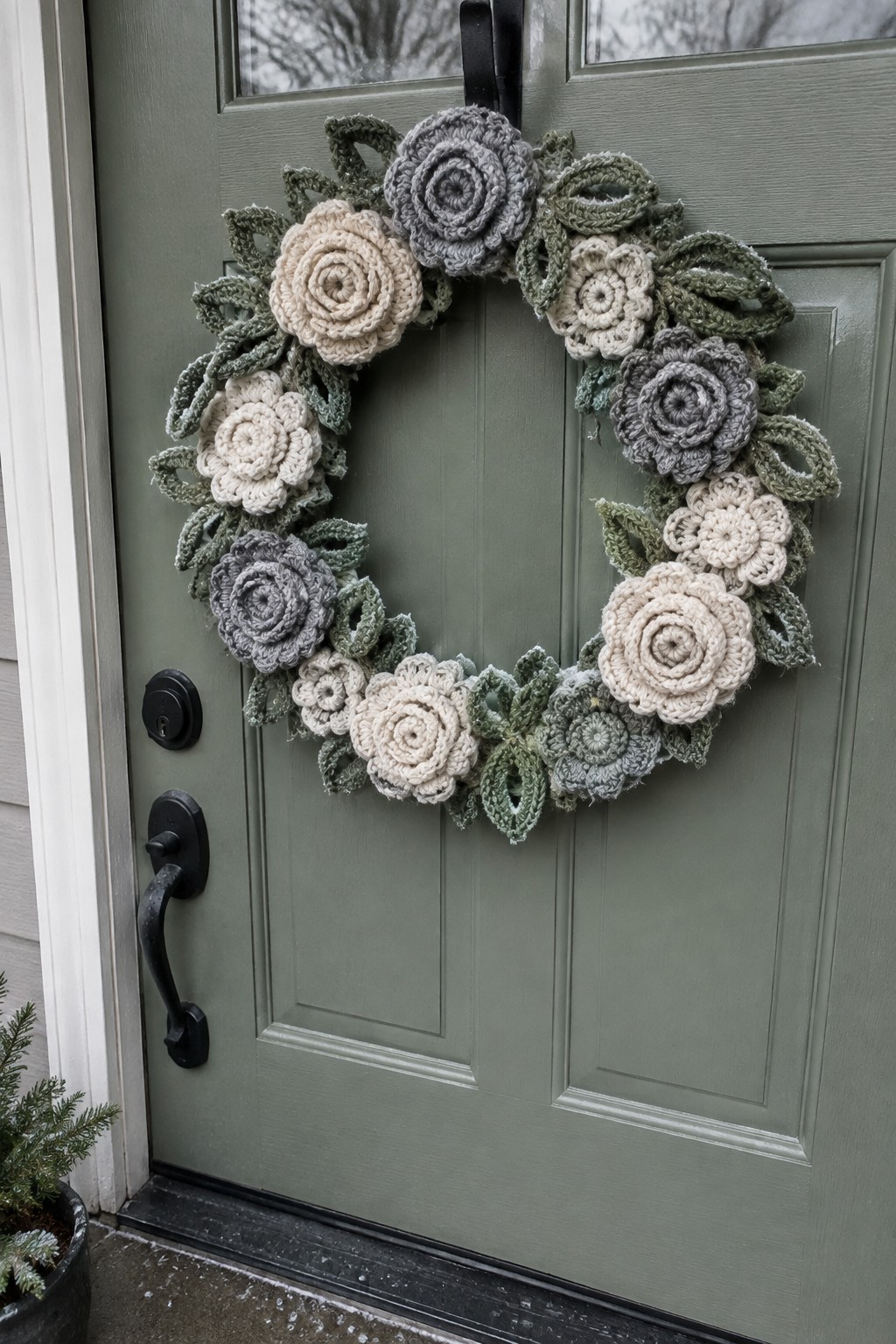 Crocheted floral wreath in beige, gray, and green on a sage door