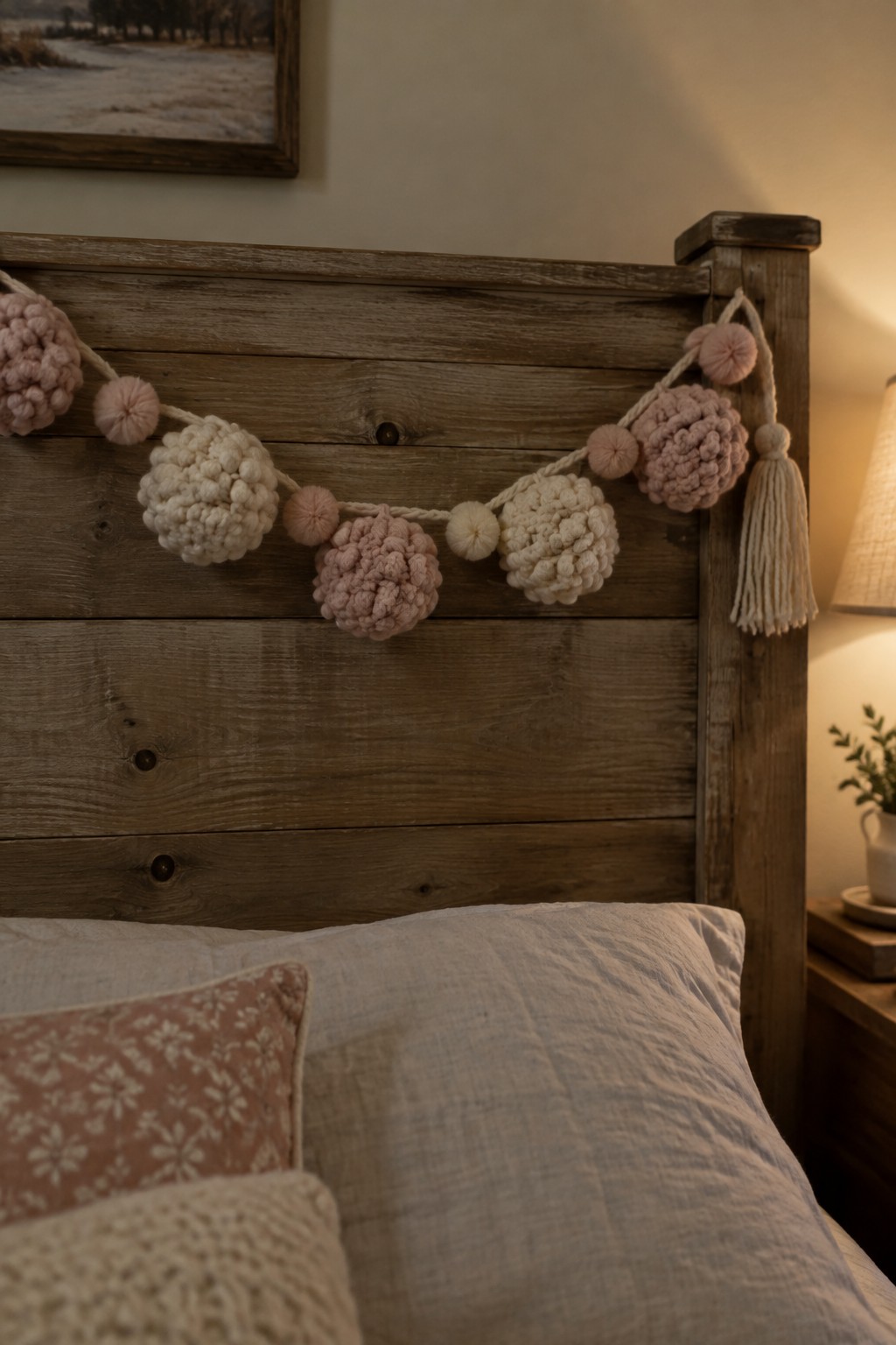Pink and cream pom-pom garland draped across rustic wooden bed headboard with pillows