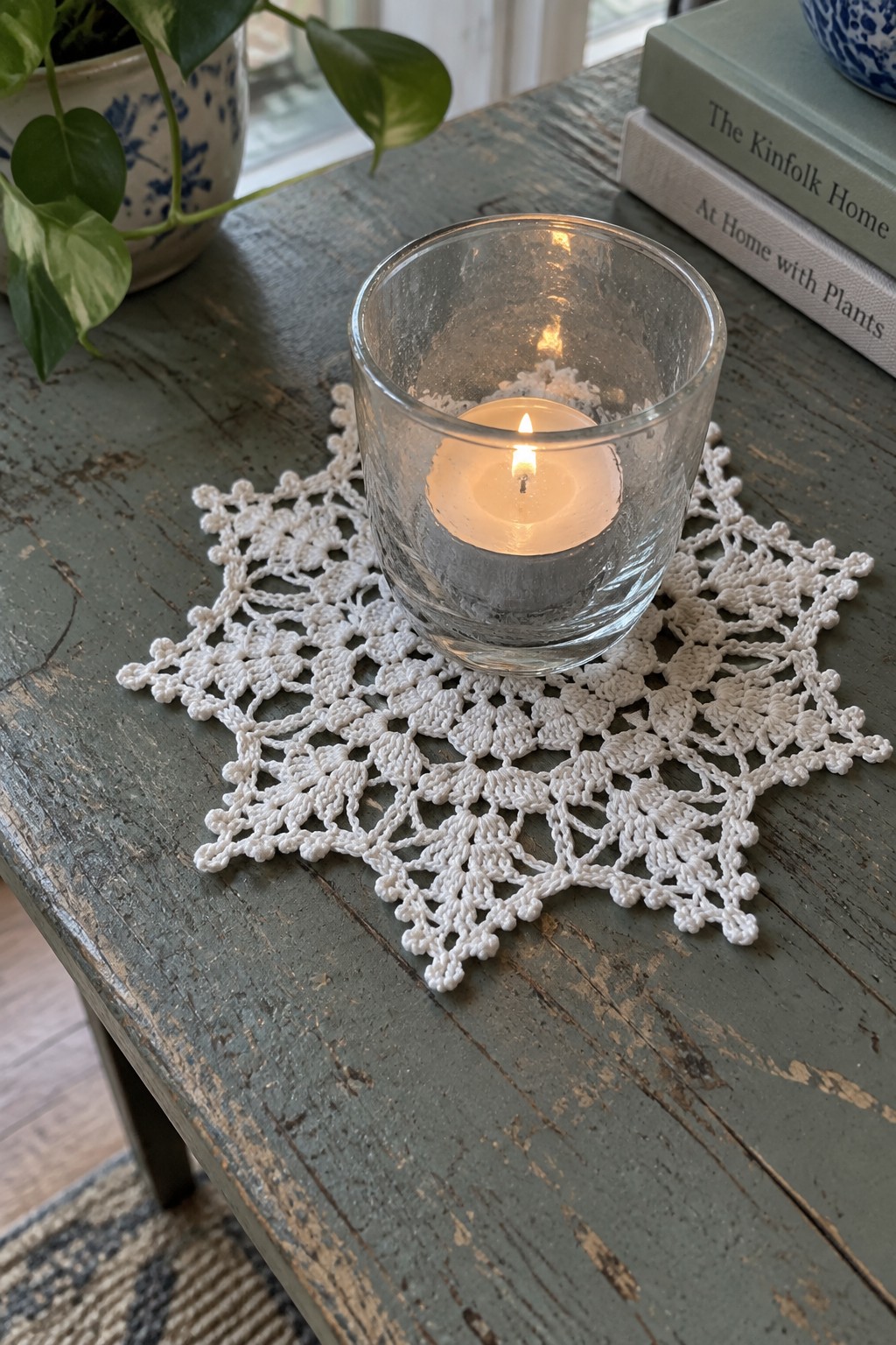 Lit candle in glass on white crocheted doily atop weathered wooden table