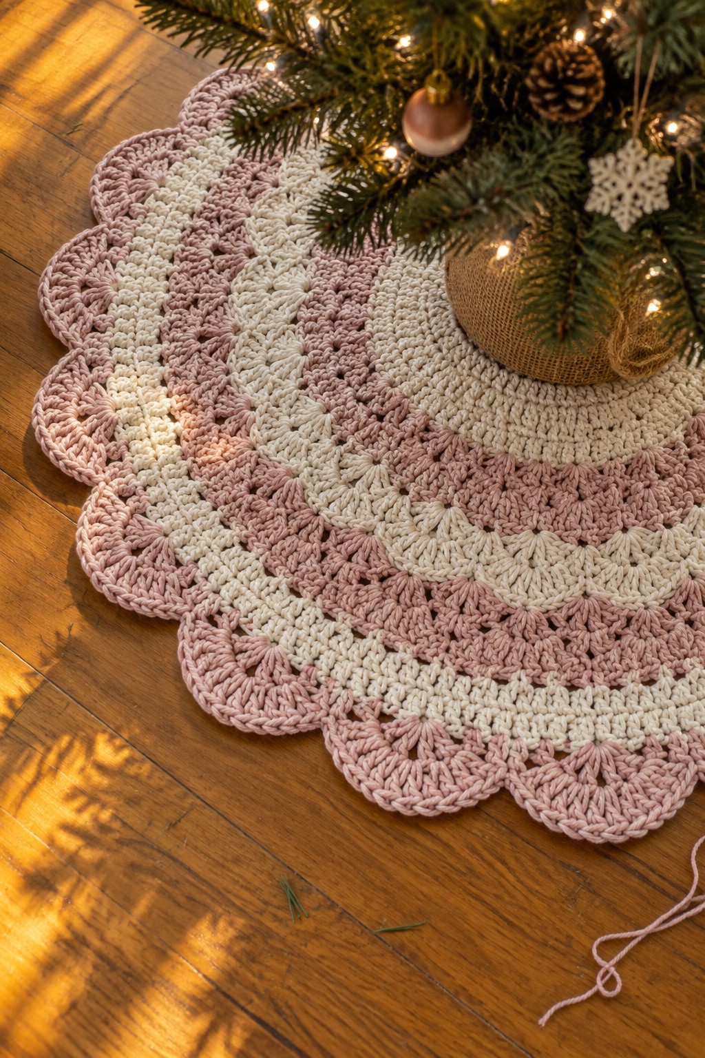 Pink and white crocheted tree skirt under a decorated Christmas tree on wood floor