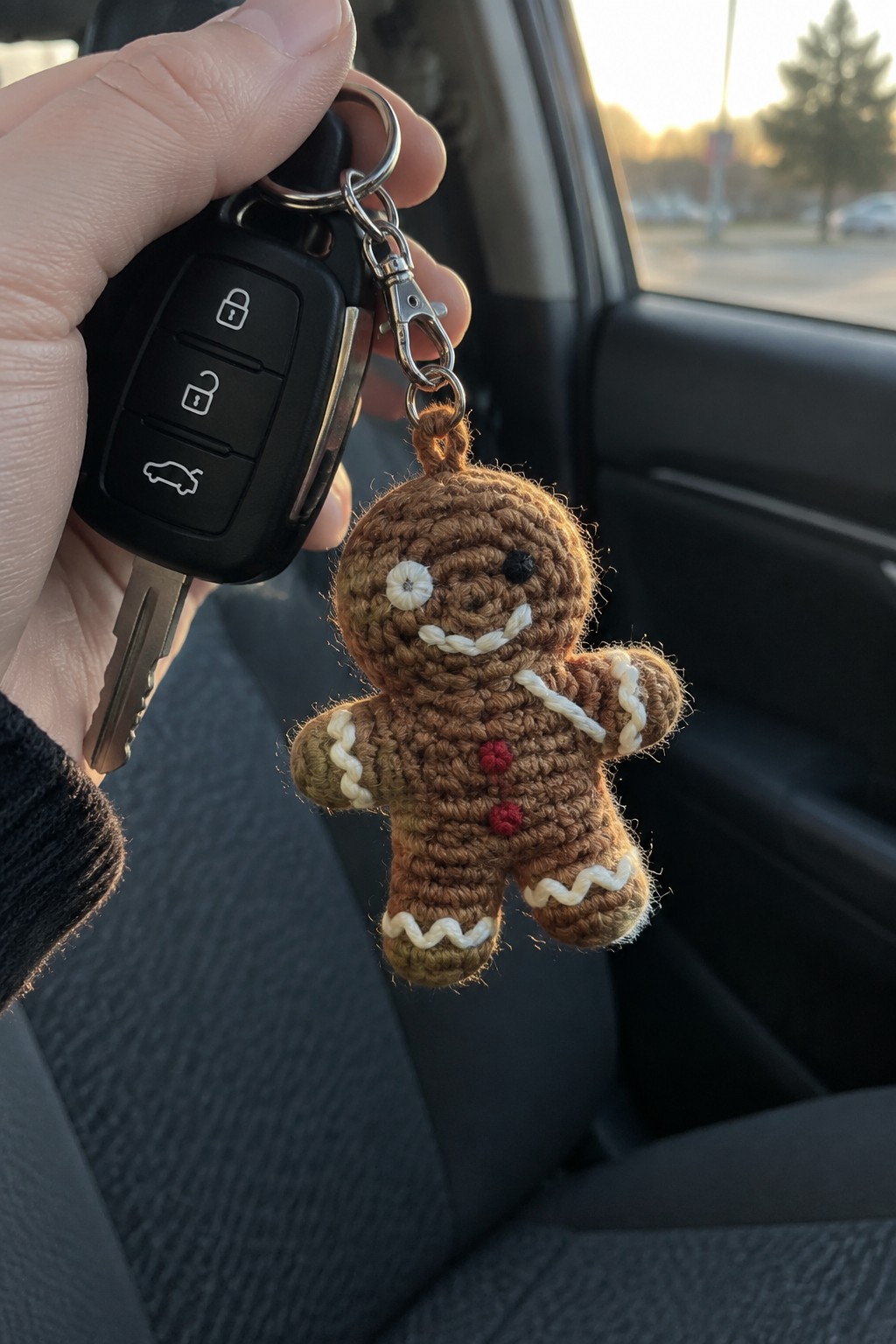 Hand holding black car key with crocheted gingerbread man keychain in vehicle