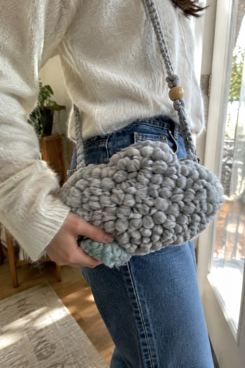 Woman in white knit sweater holding chunky gray looped-yarn handbag with braided strap