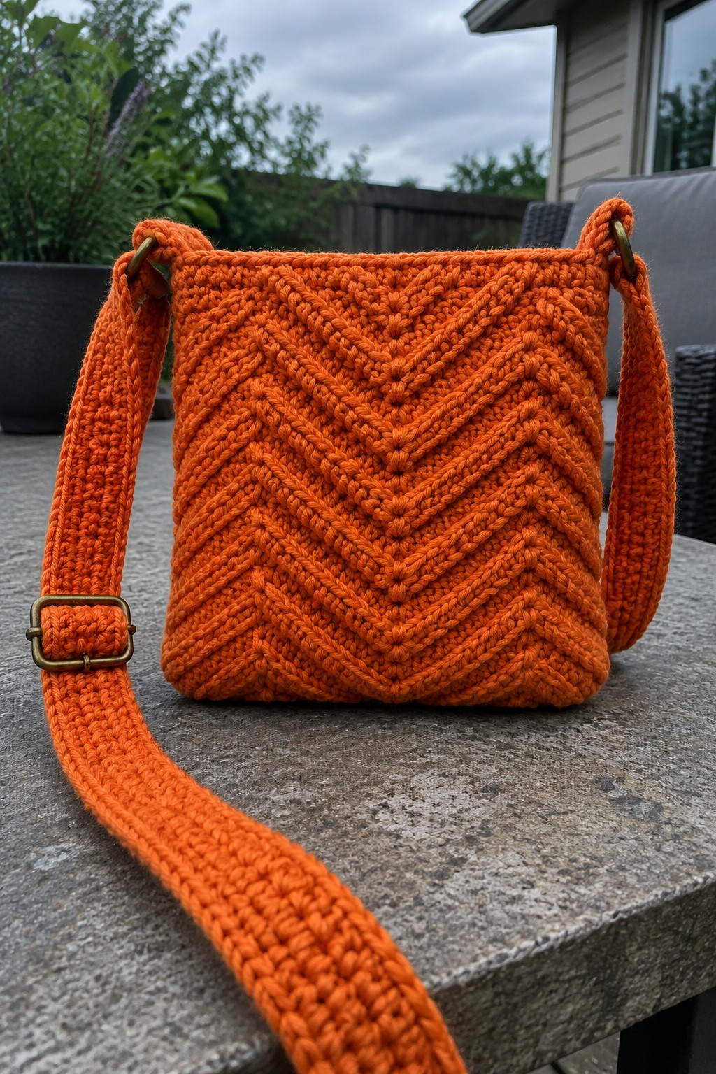 Orange crocheted crossbody bag with chevron pattern on stone table