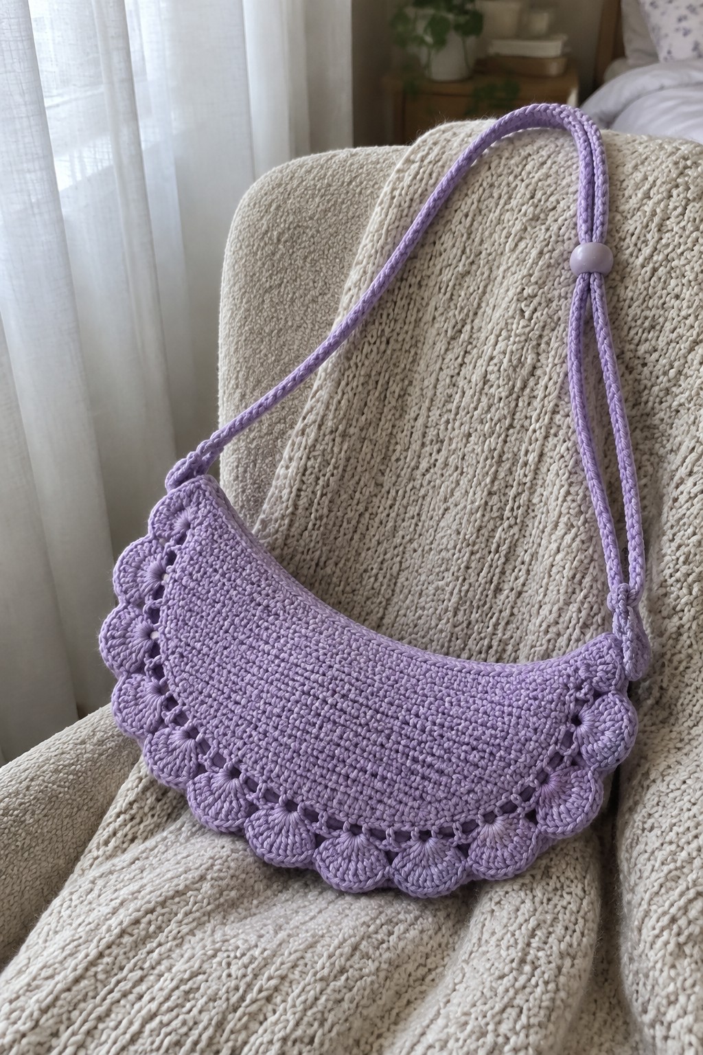 Lavender crocheted crescent bag with scalloped edge on beige knitted blanket