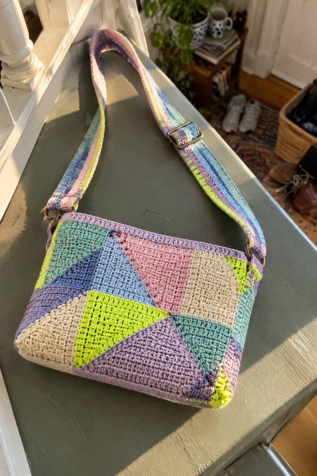 Colorful crocheted patchwork crossbody bag with striped adjustable strap on wood.