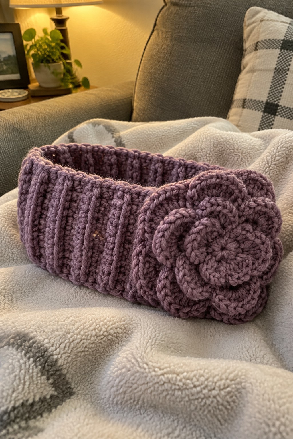 Purple crocheted headband with a flower detail lying on a white blanket.