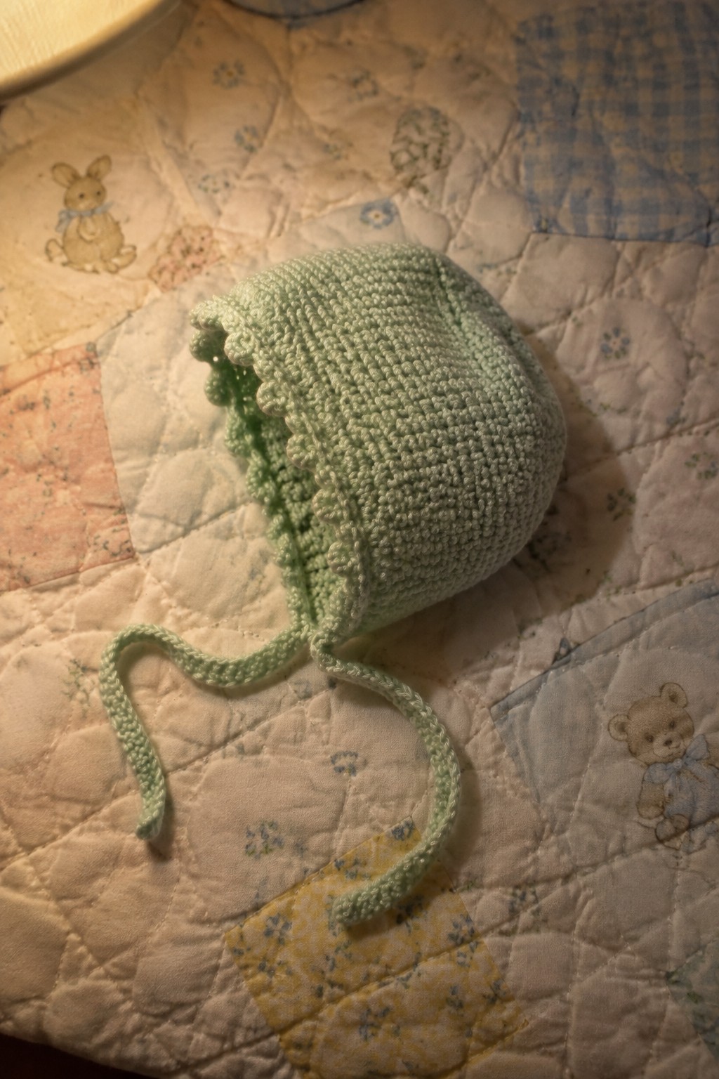 Pale green knitted baby bonnet with ties on patchwork quilt