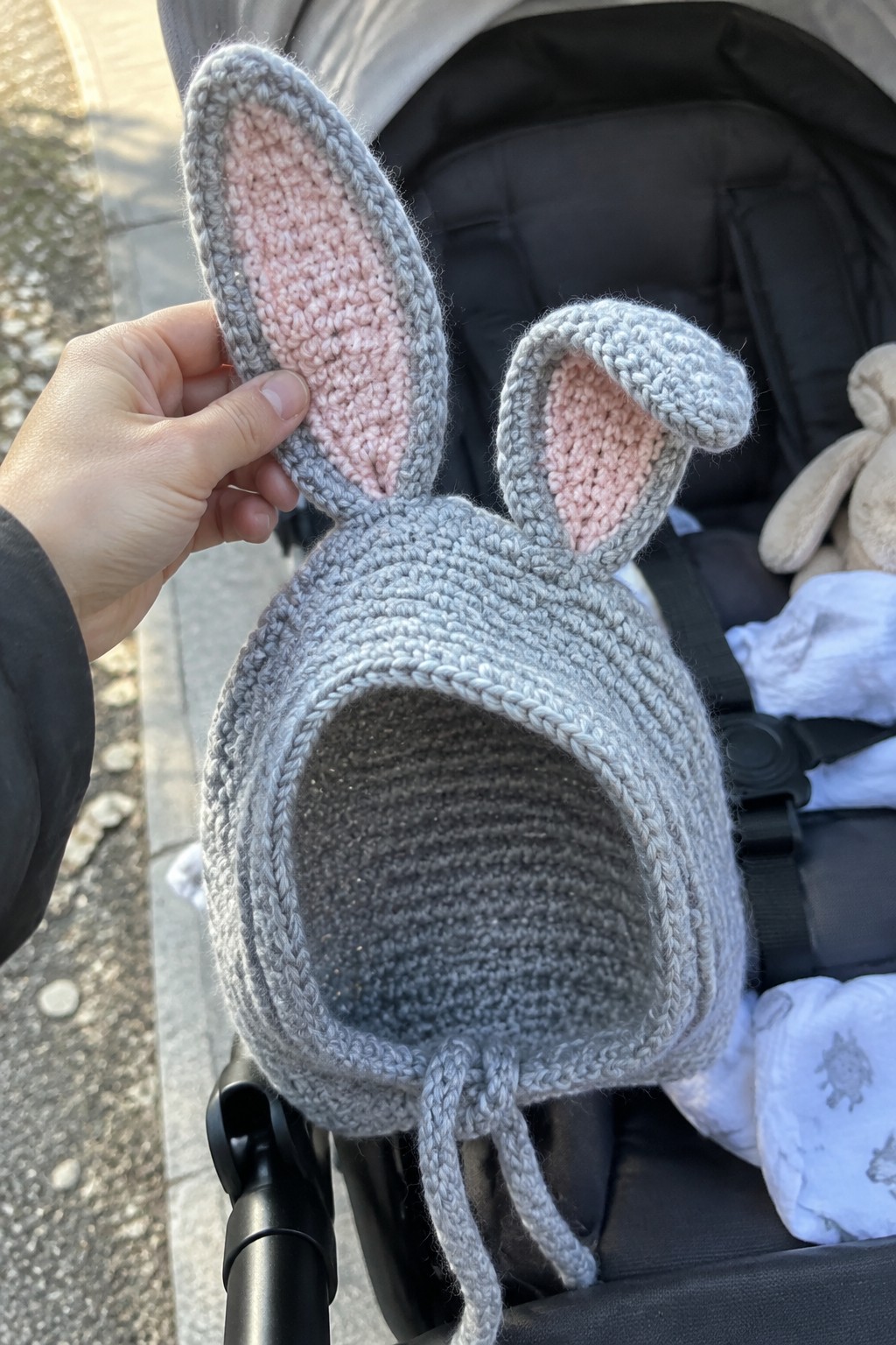 Gray knitted bunny hat with pink ears held above stroller.