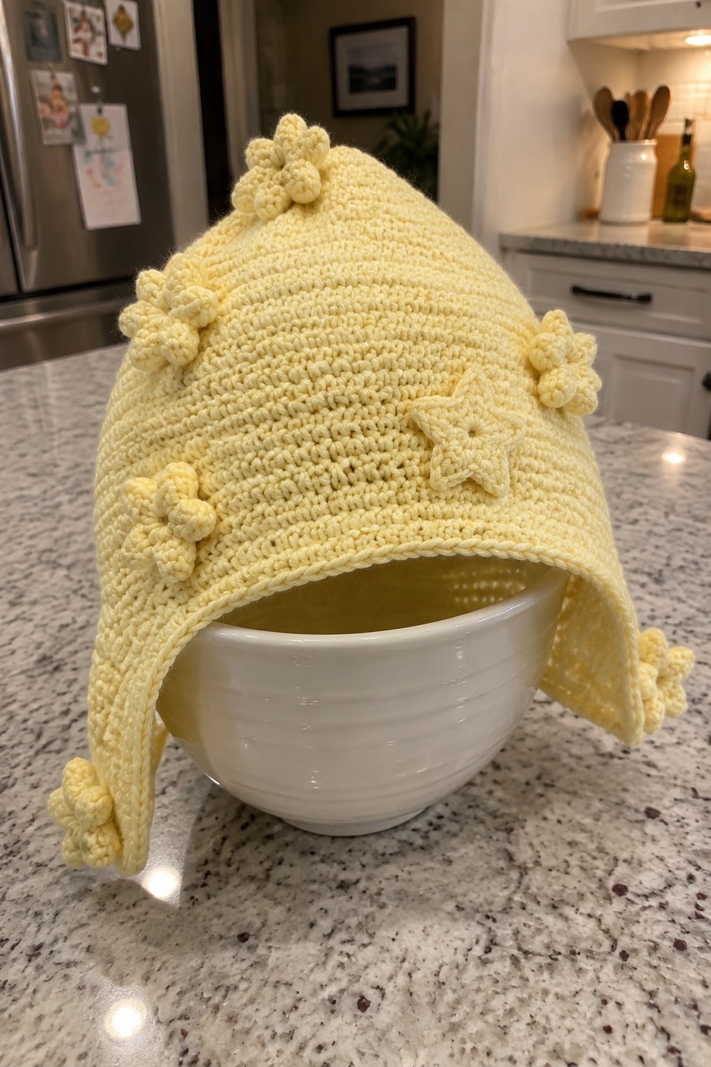 Yellow crocheted hat with flowers and star on white bowl in kitchen