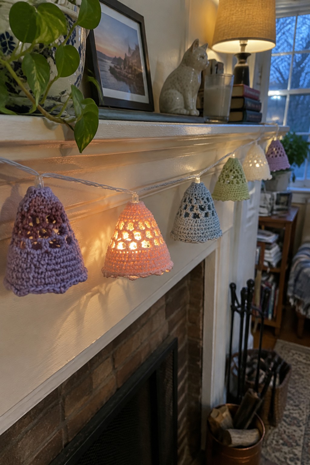 Colorful crocheted bell covers glowing on string lights along white fireplace mantel