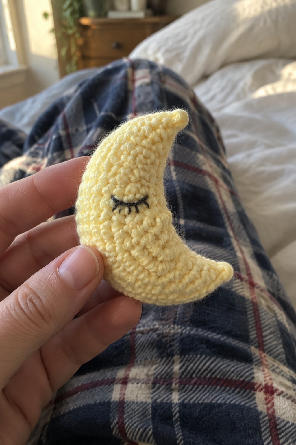 Hand holding yellow crocheted crescent moon with closed eyes on plaid pants.