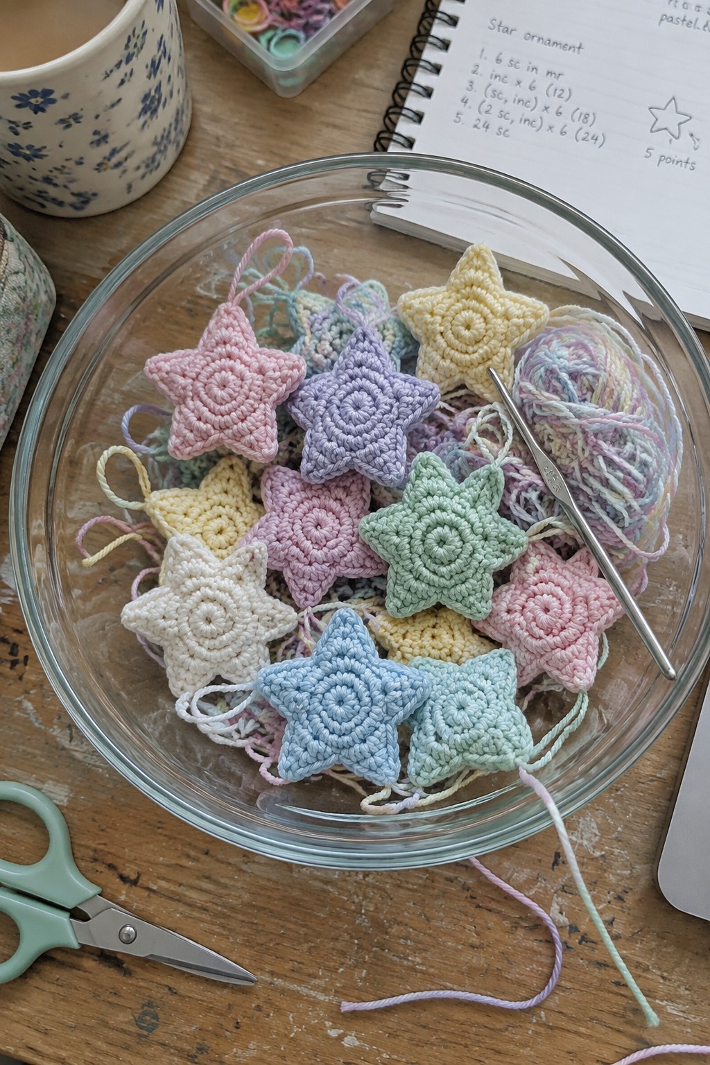 Pastel crocheted star ornaments in a glass bowl with yarn, hook, and scissors