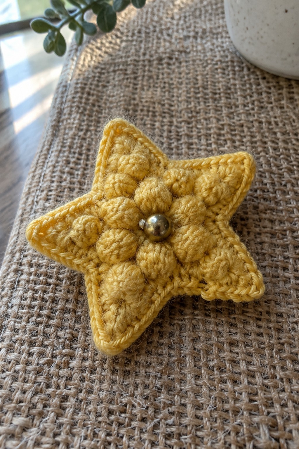 Yellow crocheted star with metallic bead center on burlap surface