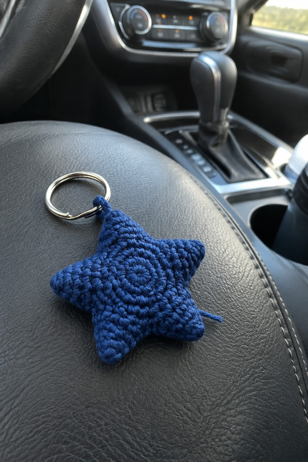 Blue crocheted star keychain on black leather car seat in vehicle.