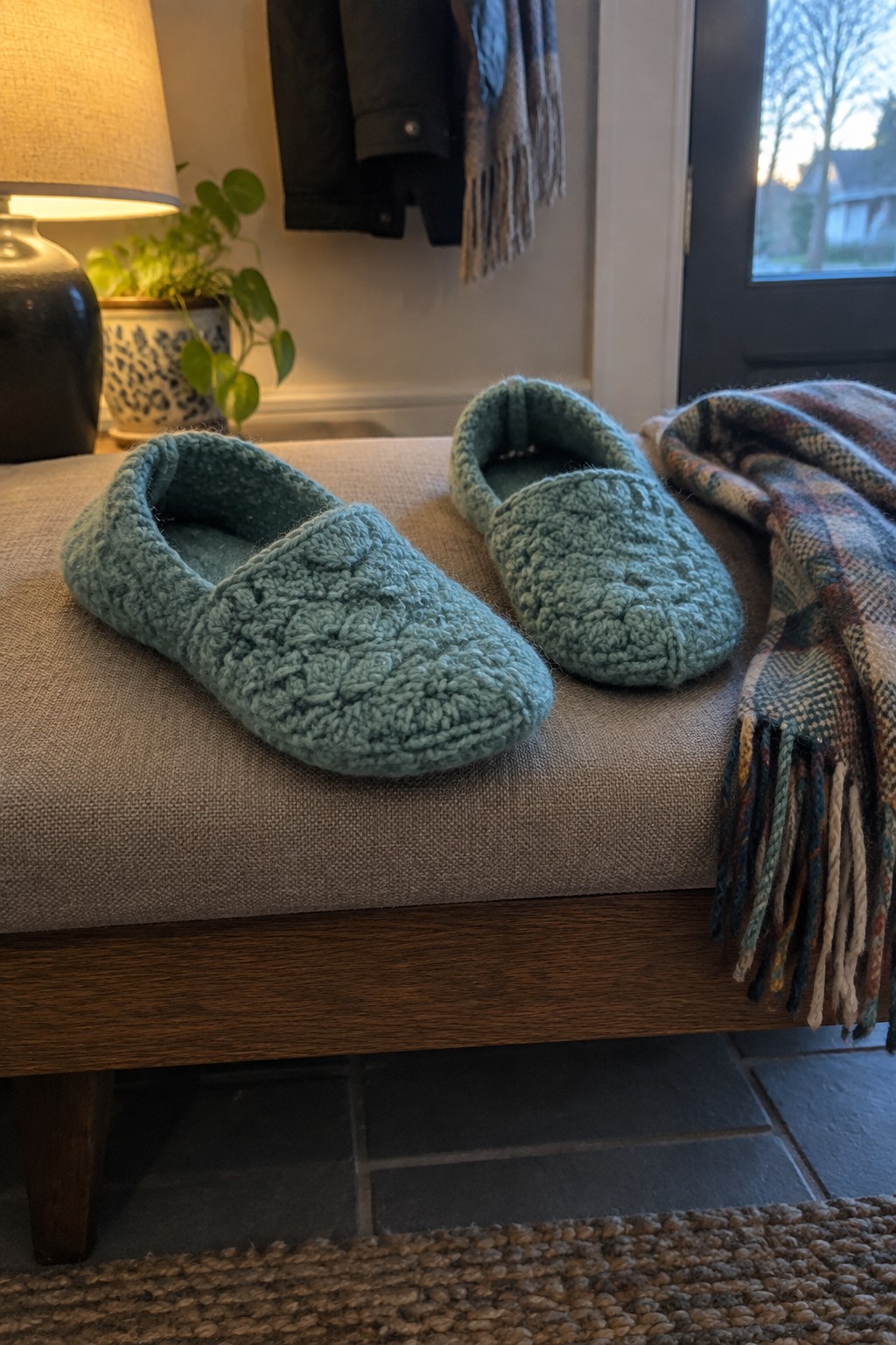 Teal knitted slippers on beige bench beside fringed plaid blanket