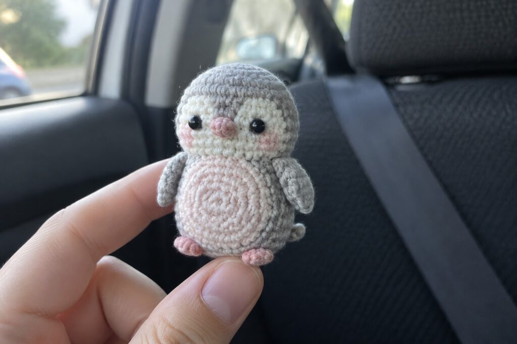 Hand holding small gray crocheted penguin with pink cheeks inside car