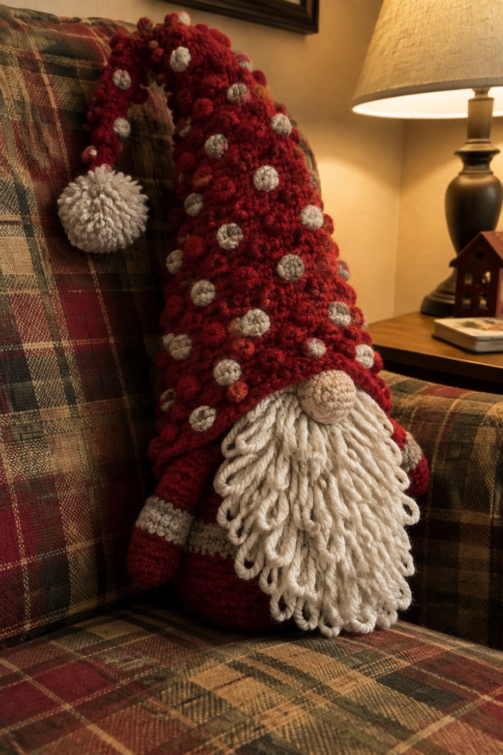 Crocheted red gnome with polka-dotted hat and shaggy white beard on plaid couch