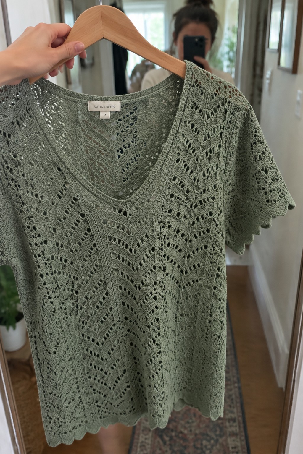 Hand holding wooden hanger with sage green lace V-neck crochet top