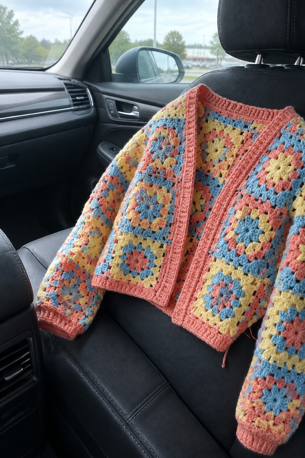 Multicolored granny square crocheted cardigan on black leather car seat