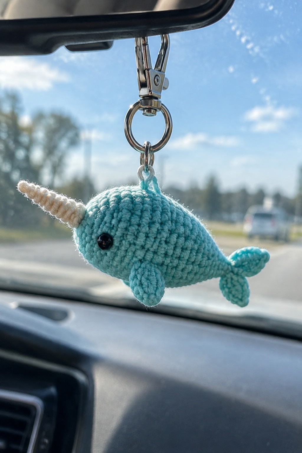 Light blue crocheted narwhal keychain with white tusk hanging from car mirror