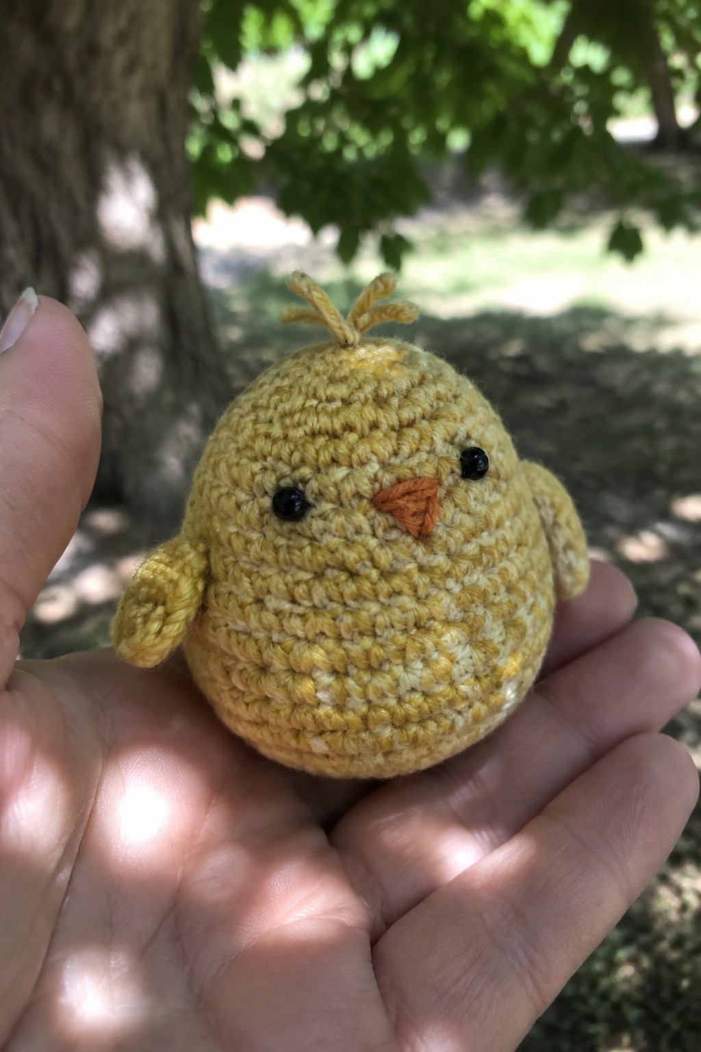A small yellow crocheted chick amigurumi held in an open hand outdoors.