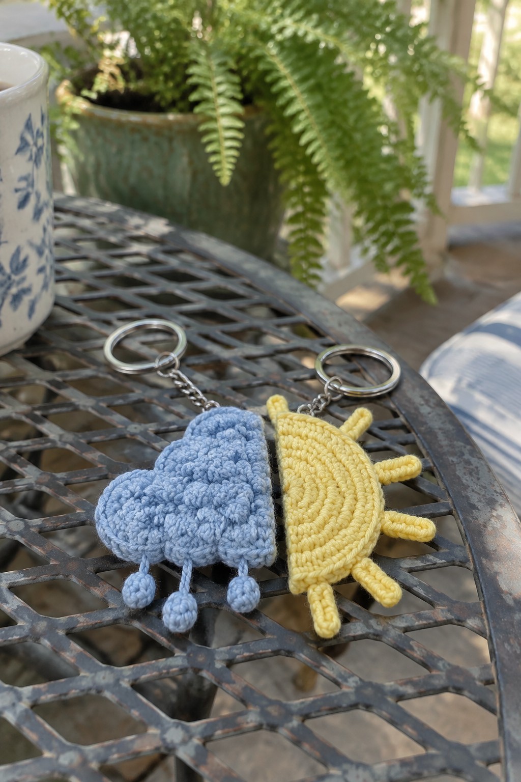 Crocheted blue cloud with raindrops and yellow sun keychains on metal table