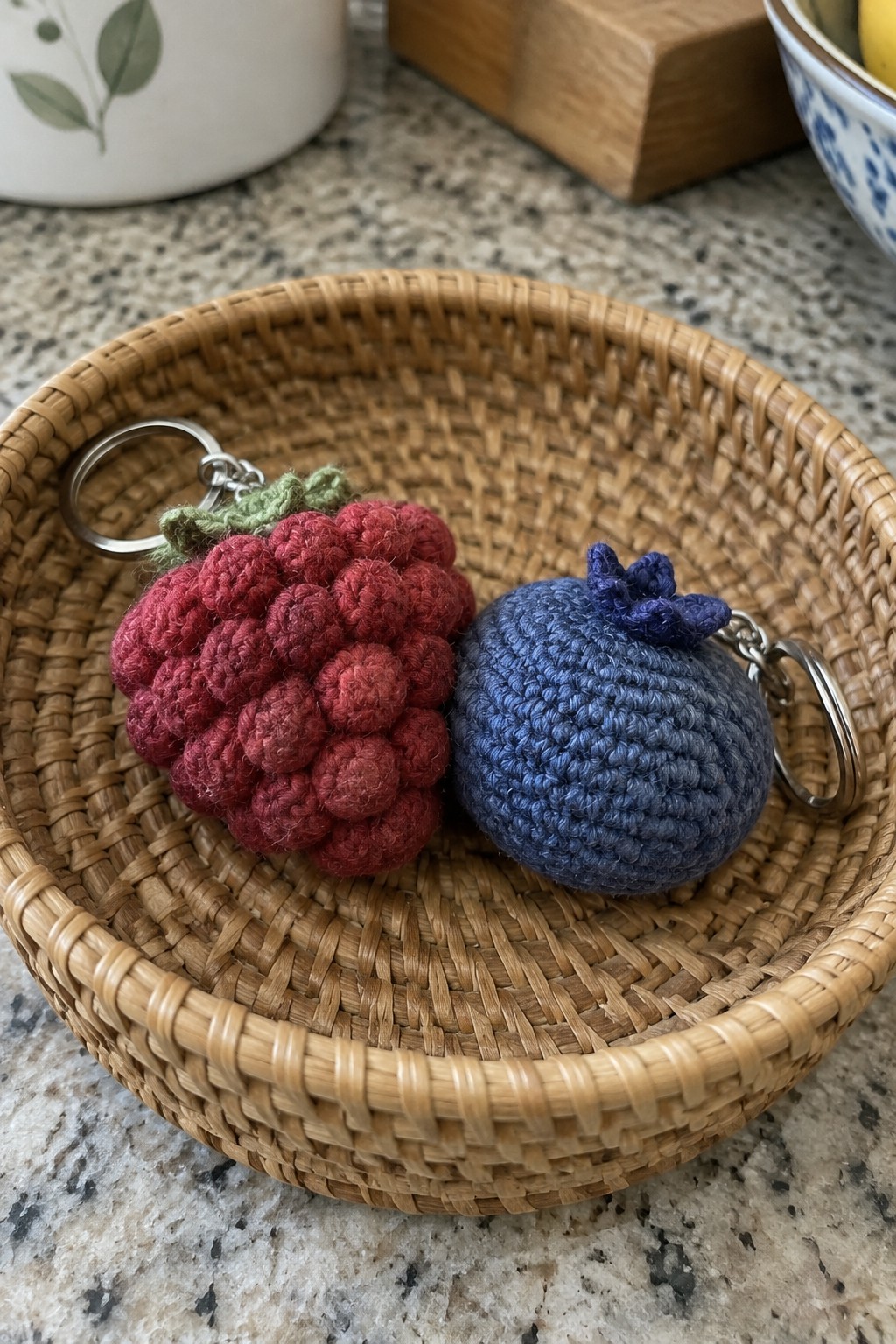 Crocheted red raspberry and blue blueberry keychains in a woven basket.