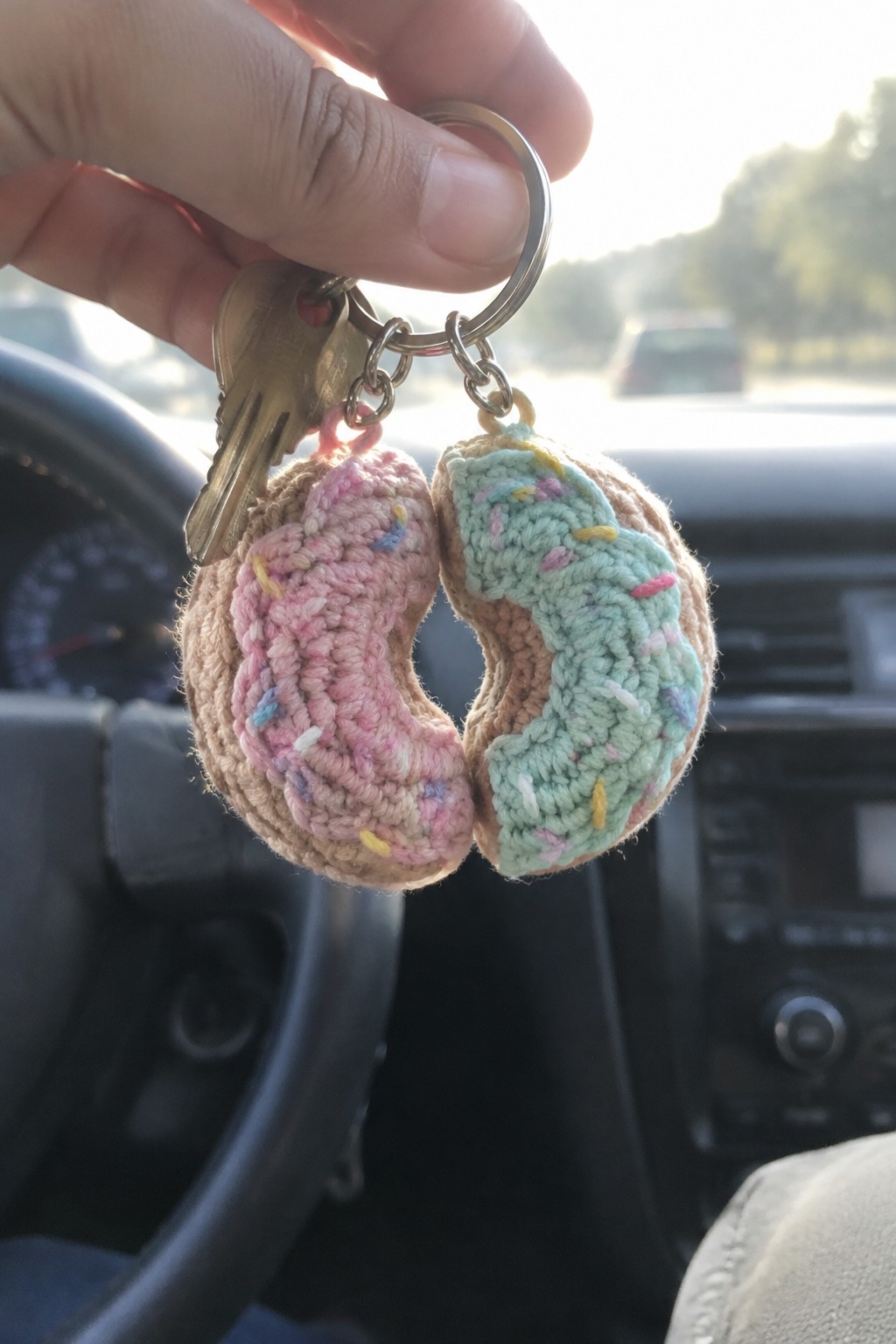 Hand holding keyring with pink and mint crocheted donut keychains inside car