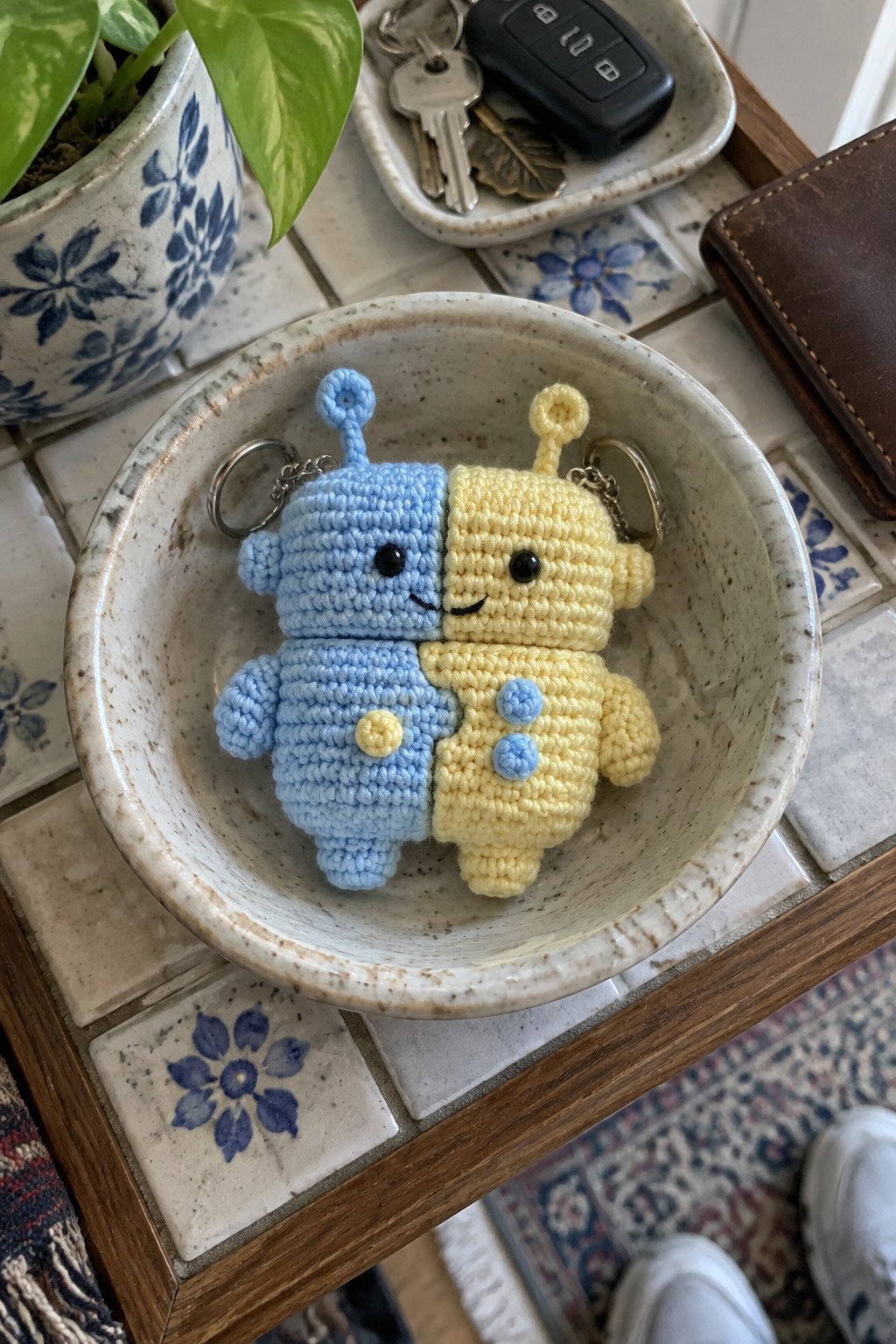 Blue and yellow crocheted robot keychains in a speckled ceramic bowl