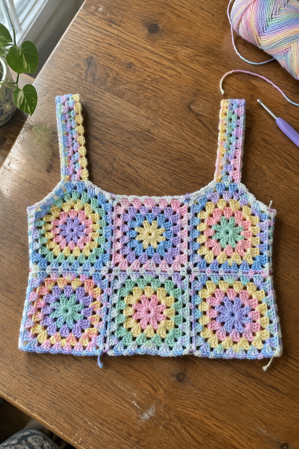 Pastel rainbow granny square crochet tank top on wooden table with yarn and hook