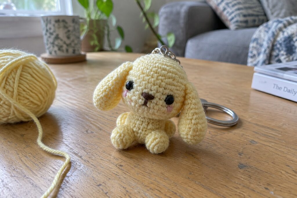 Yellow crocheted dog keychain with yarn ball on wooden table