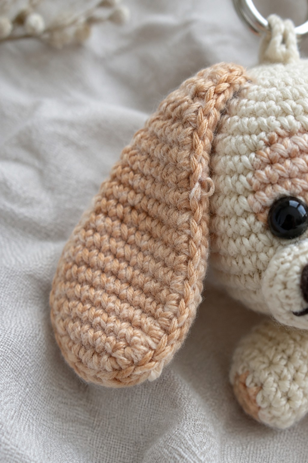 Close-up of tan crocheted floppy ear on cream amigurumi keychain with black eye.