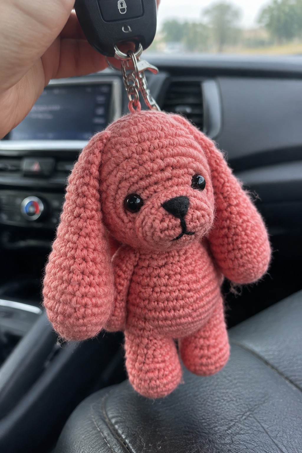 A small pink crocheted dog keychain with long floppy ears hangs from a car key inside a vehicle.