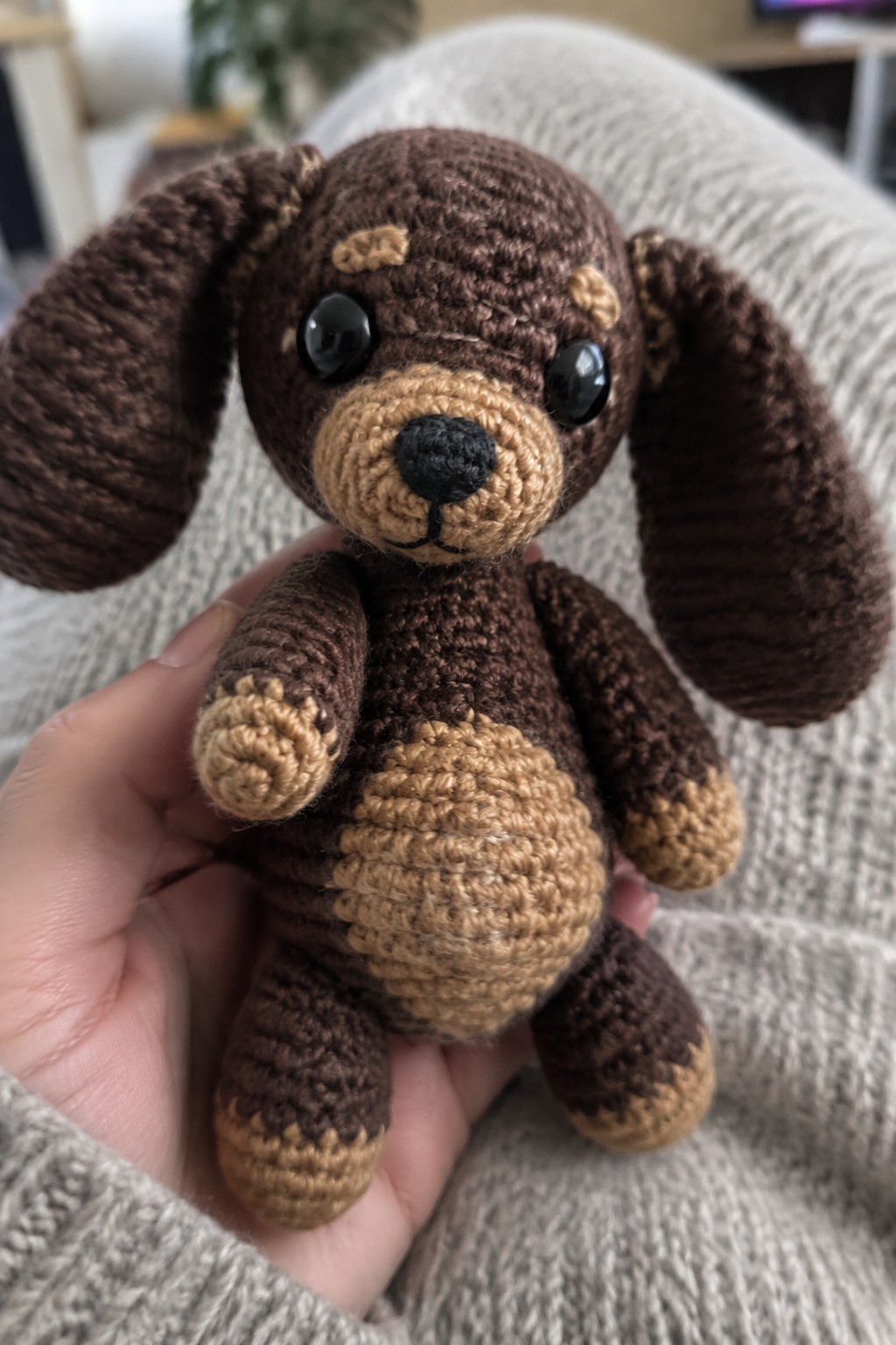 Hand holding brown crocheted dog with tan muzzle, ears, paws and belly patch