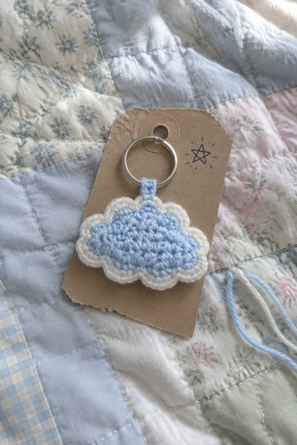 Light blue crocheted cloud keychain on silver ring with star tag on quilt