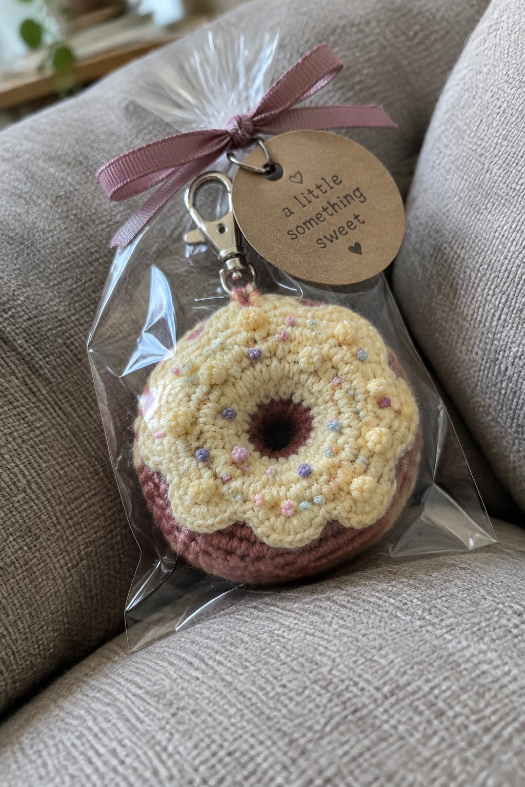 Crocheted yellow donut keychain with sprinkles in clear bag tied with pink ribbon and tag.