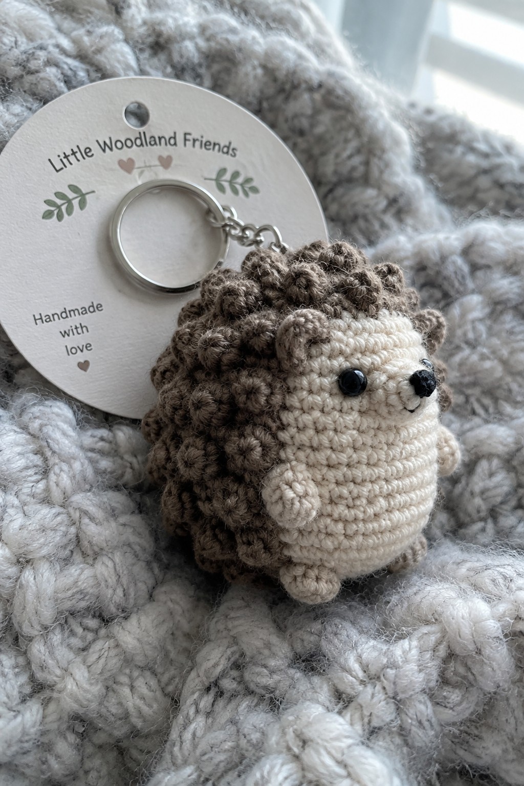 Crocheted brown and beige hedgehog keychain with tag on chunky gray knit fabric