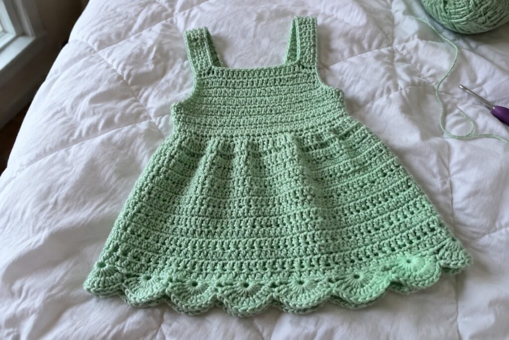 16 Crochet Sundresses With Scalloped Hems Mint green crocheted dress with scalloped hem on white quilt beside yarn and hook
