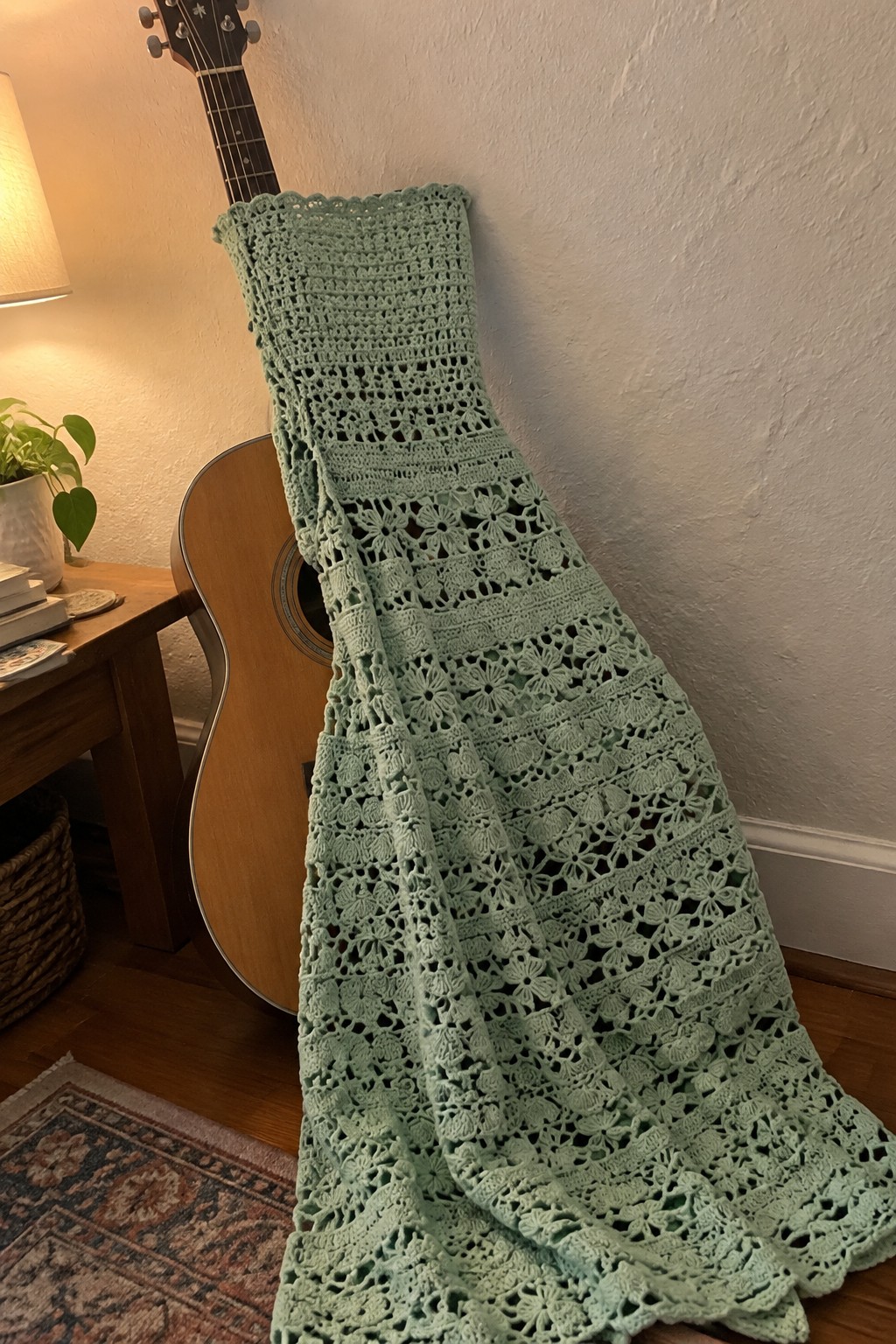 Mint green floral crochet blanket draped over acoustic guitar in cozy room
