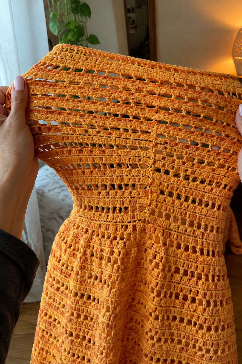 Hands stretching an orange-yellow crocheted lace top with openwork pattern.