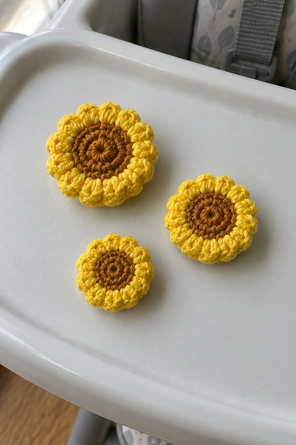 Three crocheted yellow sunflowers with brown centers on a white tray.