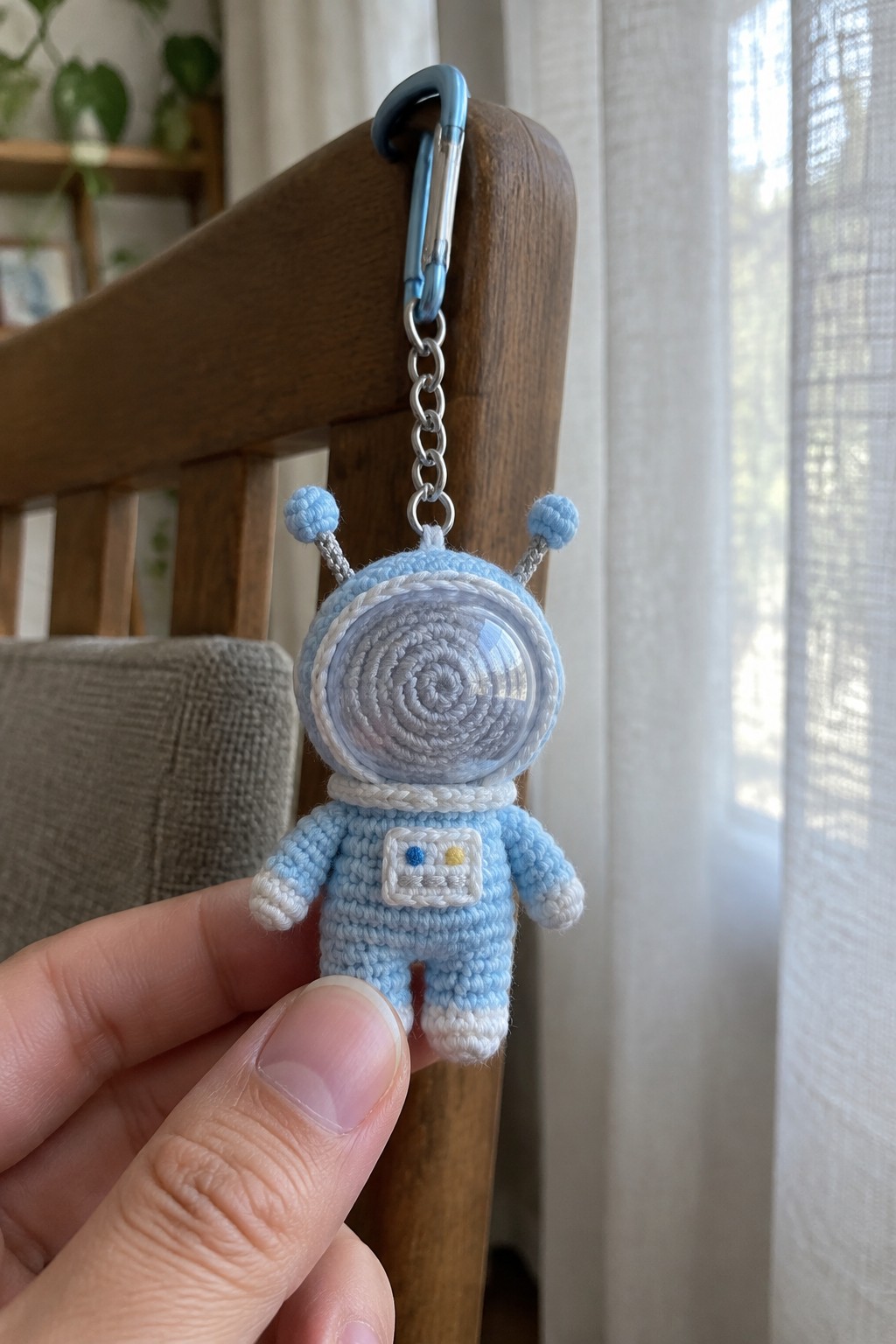 Hand holding light blue crocheted astronaut keychain with clear helmet and carabiner.