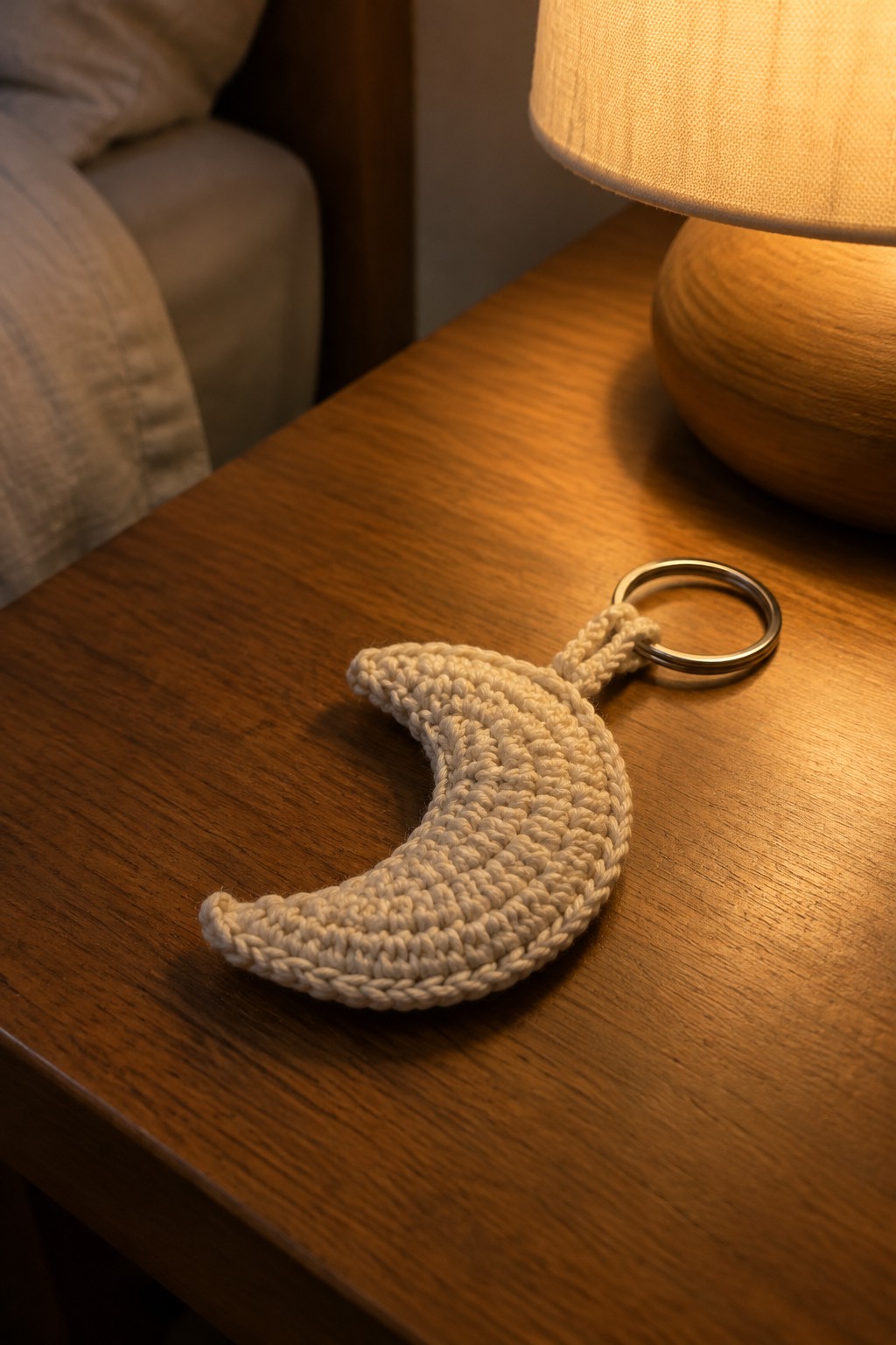 A crocheted crescent moon keychain with a metal ring on a wooden surface.