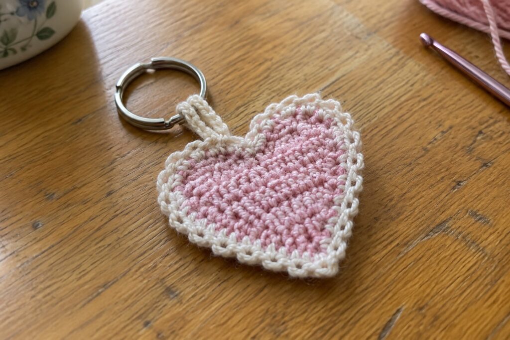18 Flat Crochet Keychain Ideas Using Simple Shapes and Basic Stitches Pink crocheted heart keychain with white border on silver ring atop wooden table