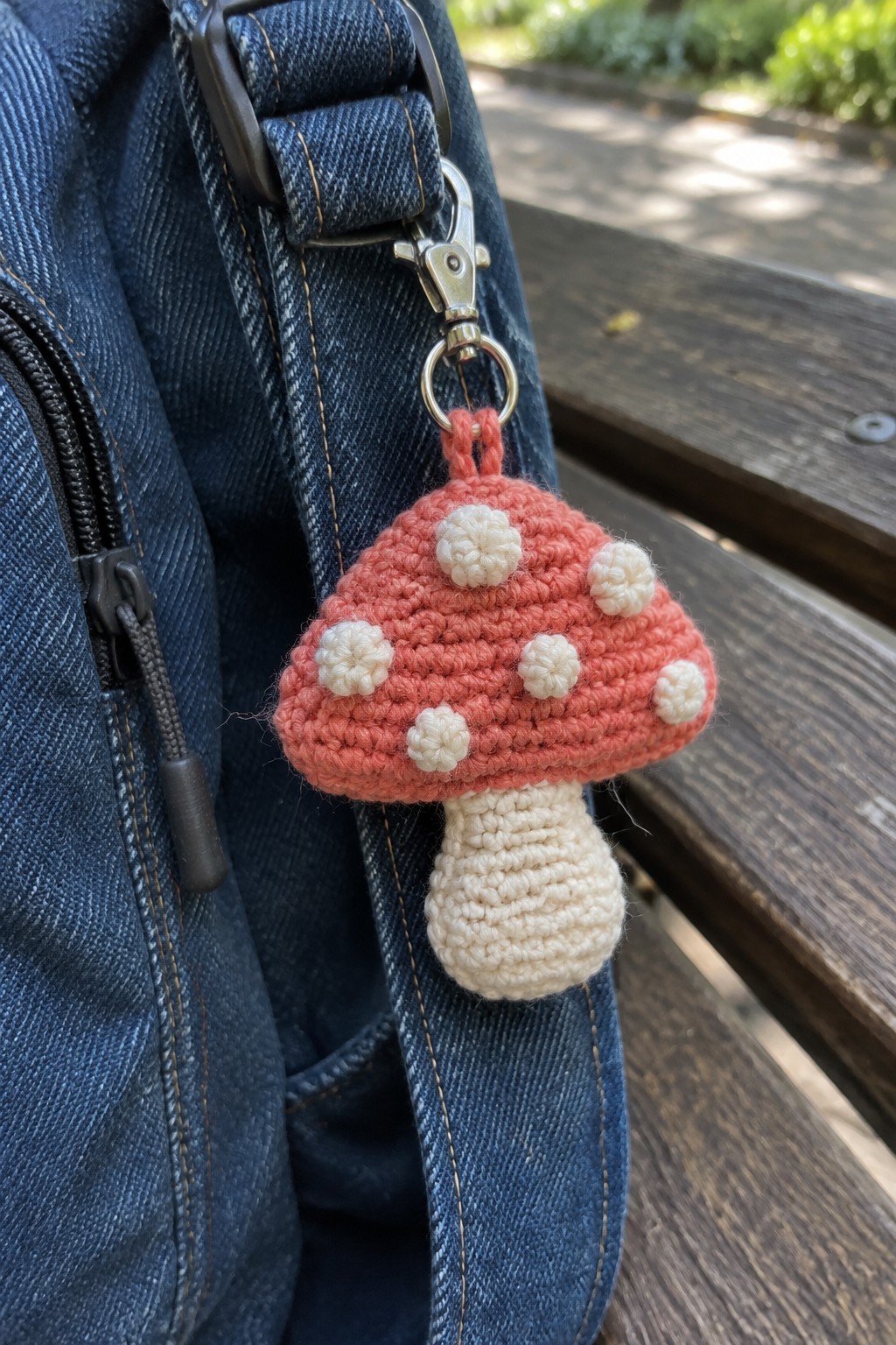 Crocheted pink mushroom keychain with white spots on blue denim bag